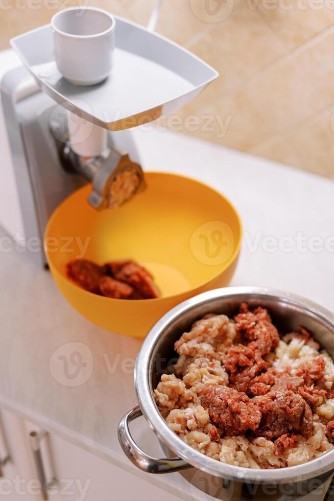 Pot with minced meat stands near an electric meat grinder with a bowl on the table photo
