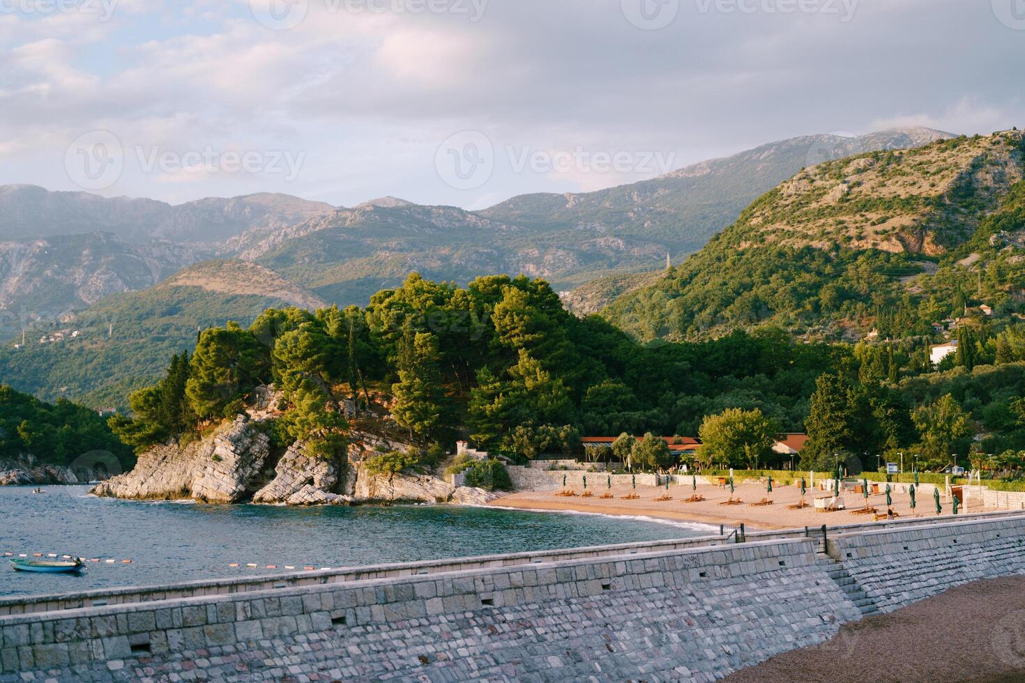 View from the stone isthmus to the sandy beach at the foot of the green mountain range photo
