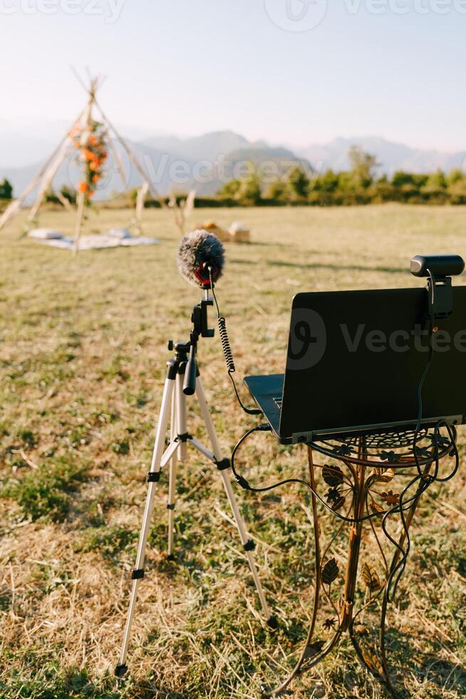 Laptop with a webcam and a microphone on a stand stands in front of a wedding arch on a green meadow photo