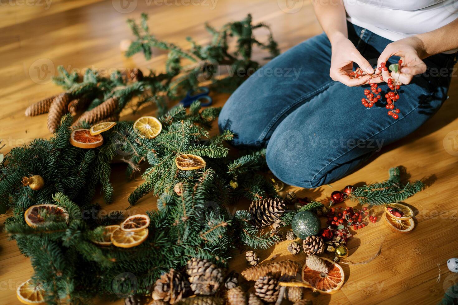 Decorator holds in his hands a sprig of red berries for a Christmas wreath lying on the floor. Cropped photo