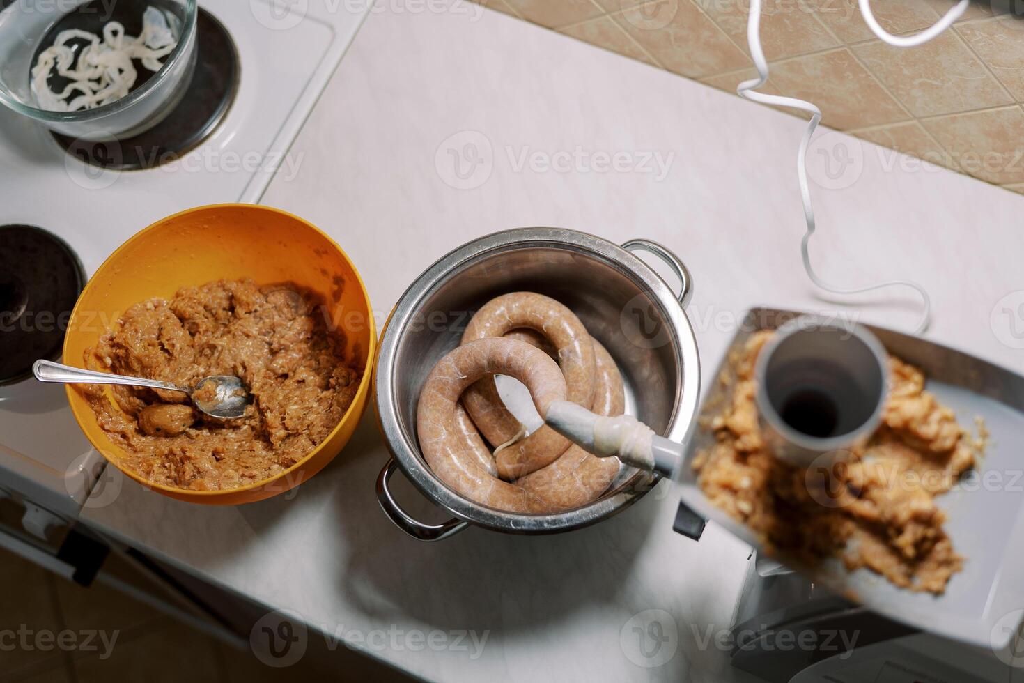 Bowl of minced meat stands near an electric meat grinder making sausage in the kitchen photo