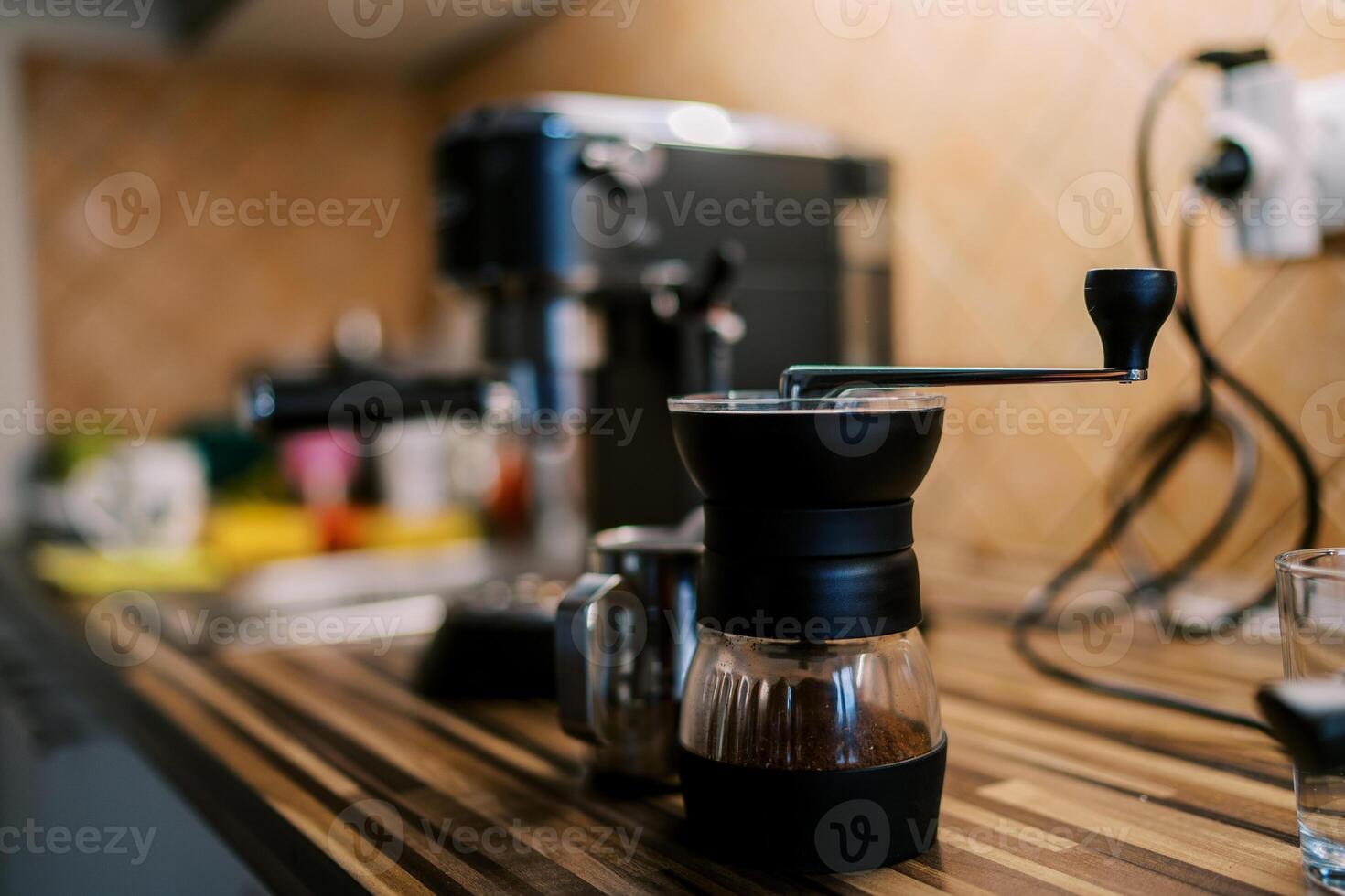 Manual coffee grinder with ground coffee stands on the table near the coffee machine photo
