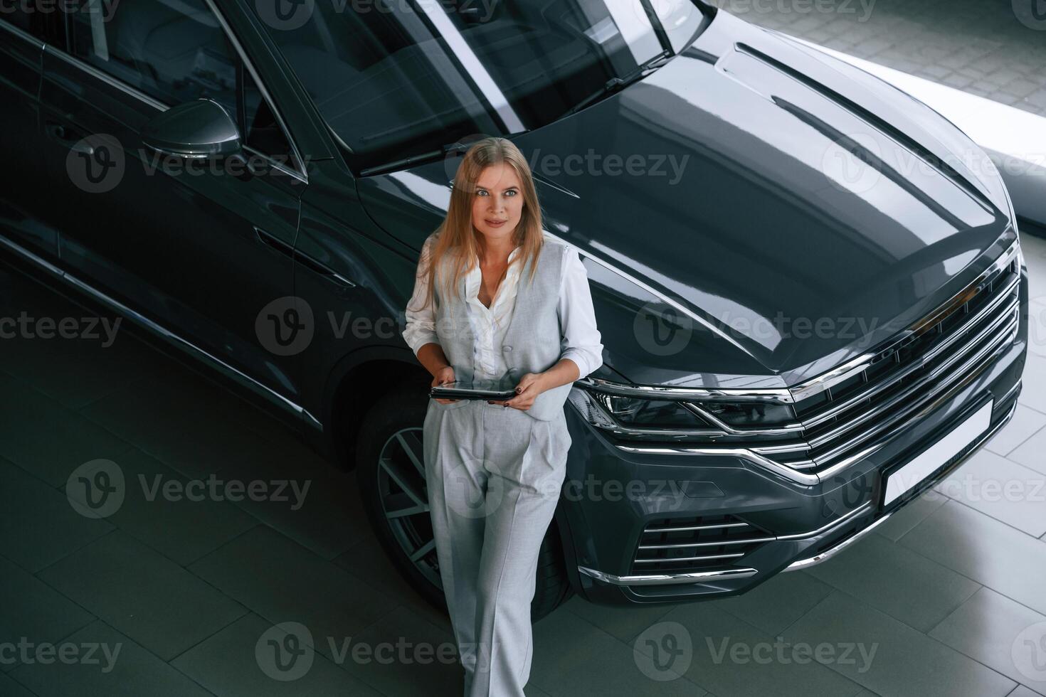 With tablet in hands. Woman in formal clothes is in the car dealership photo
