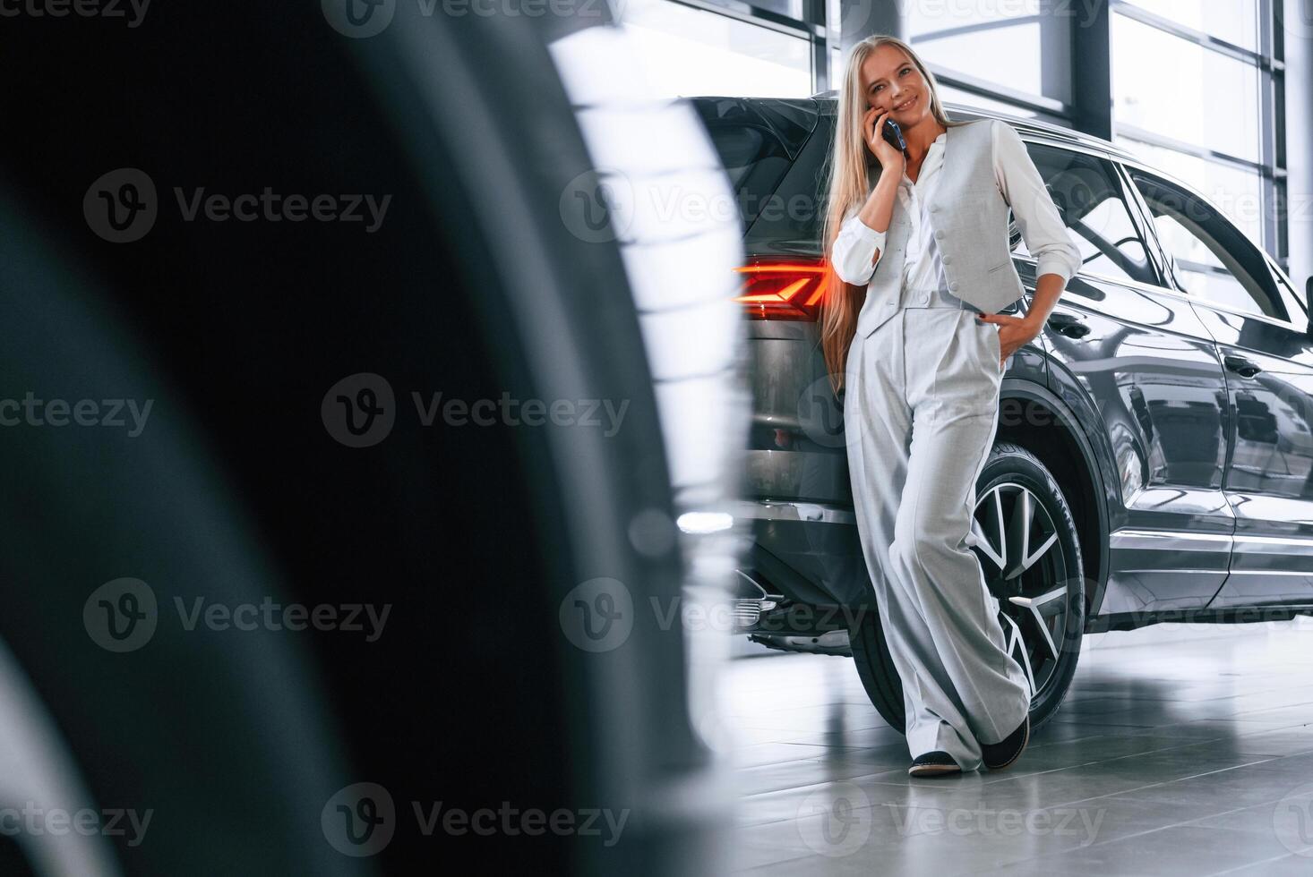 Talking by phone,. Woman in formal clothes is in the car dealership photo