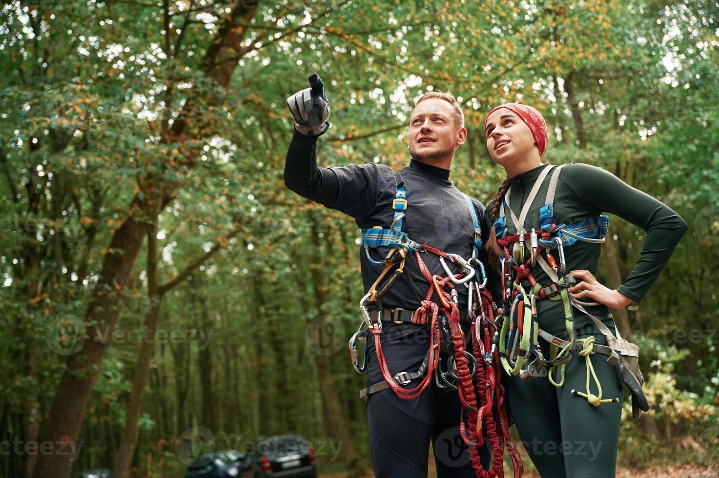 Male, is ,showing something by hand and talking. Man and woman doing climbing in forest with use of safety equipment photo