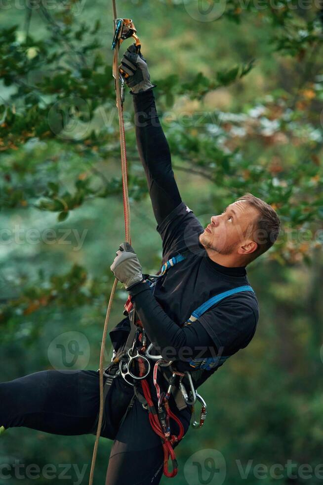 Man is doing climbing in the forest by use of safety equipment photo
