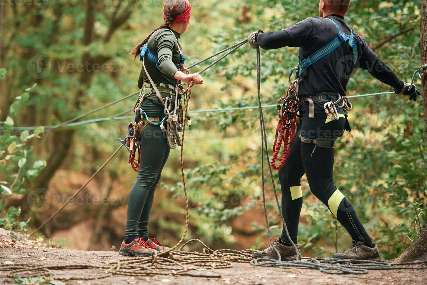 Preparing ,,the ropes. Man and woman doing climbing in forest with use of safety equipment photo
