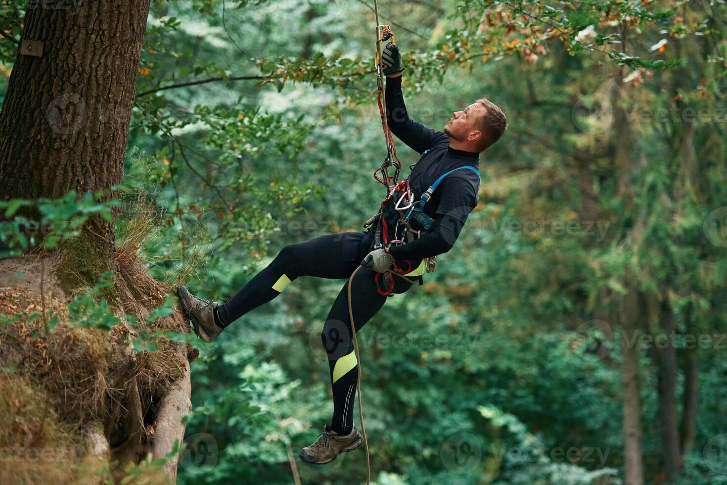 Hanging ,on, a rope. Man is doing climbing in the forest by use of safety equipment photo