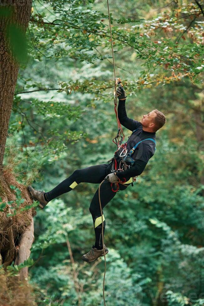 Hanging, on a rope. Man is, doing climbing in the forest by use of safety equipment photo