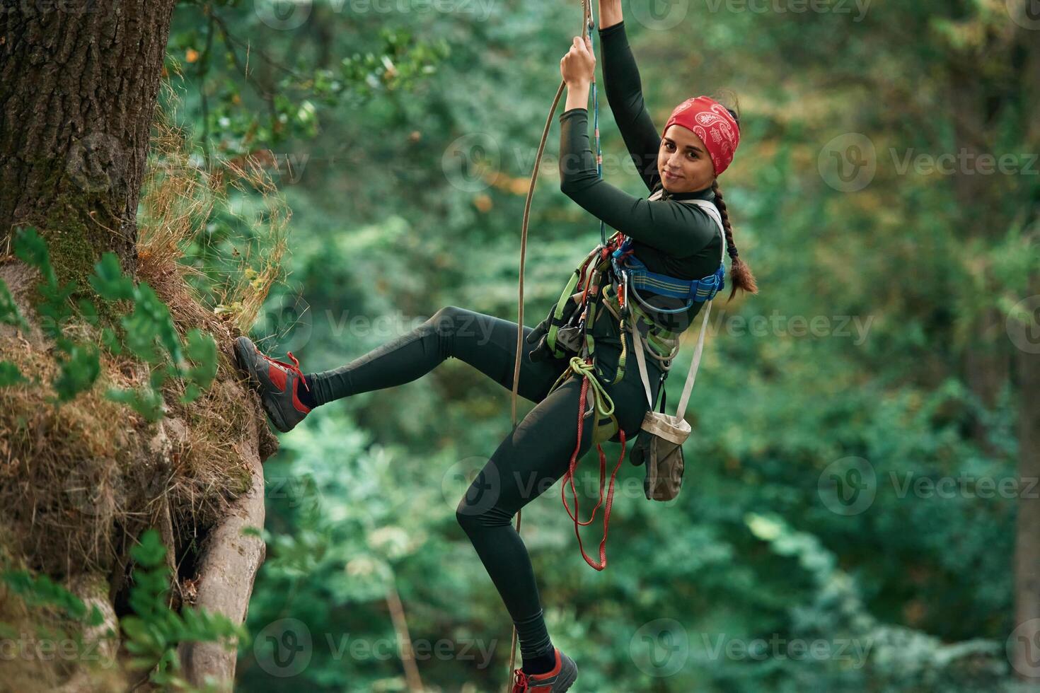 Looking, to, the side, hanging on the rope. Woman is doing climbing in the forest by the use of safety equipment photo