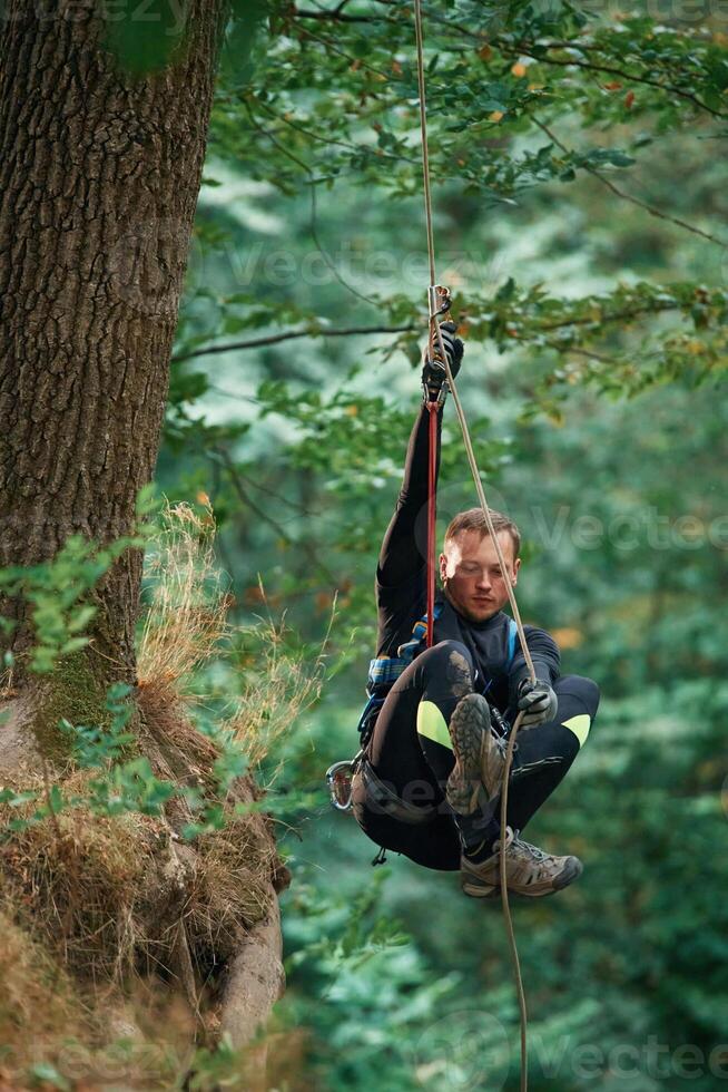 Activity, hanging on a rope. Man is doing climbing in the forest by use of safety equipment photo