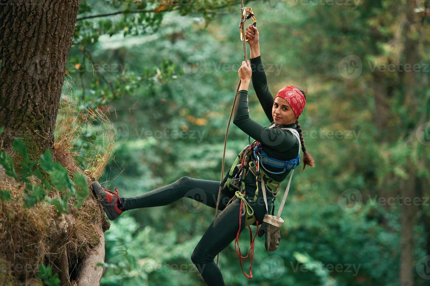 Looking to, the side, hanging on, th,e rope. Woman is doing climbing in the forest by the use of safety equipment photo