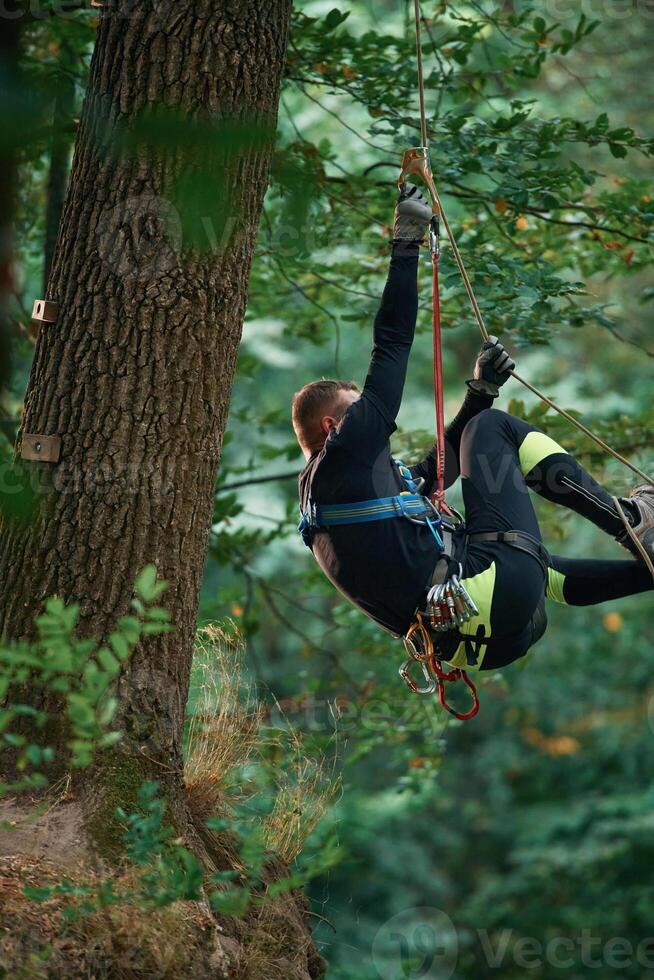 Activity, hanging, on a rope. Man is doing climbing in the forest by use of safety equipment photo