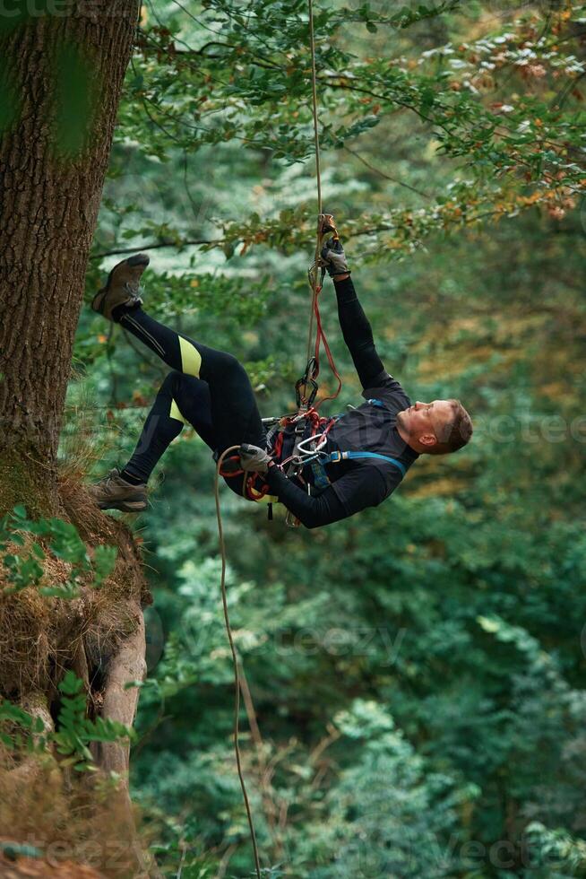 Hanging, on, a rope. Man is doing climbing in the forest by use of safety equipment photo