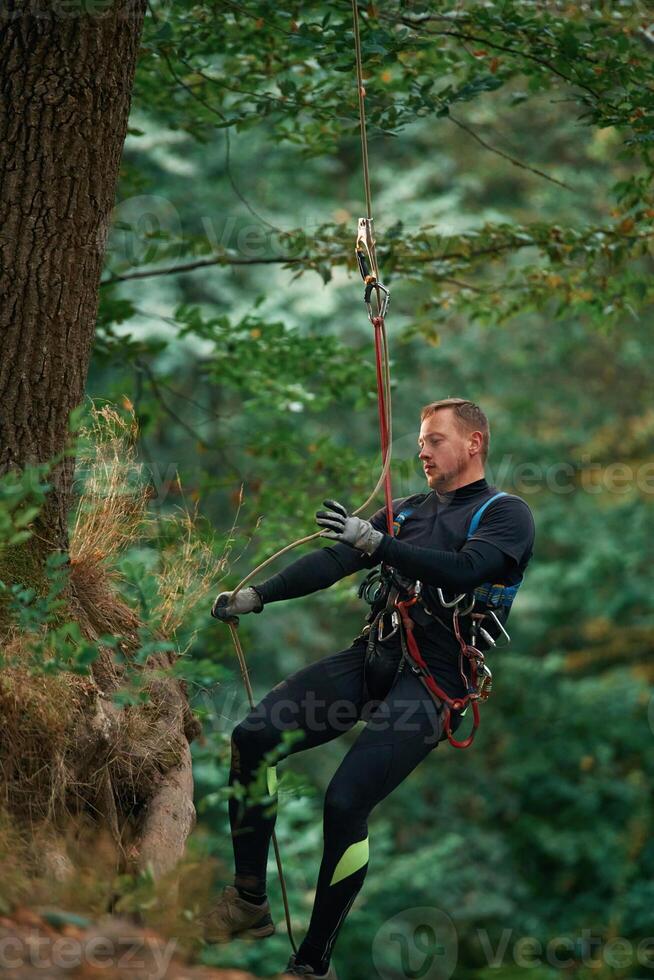 Activity, hanging on a ,rope. Man is doing climbing in the forest by use of safety equipment photo