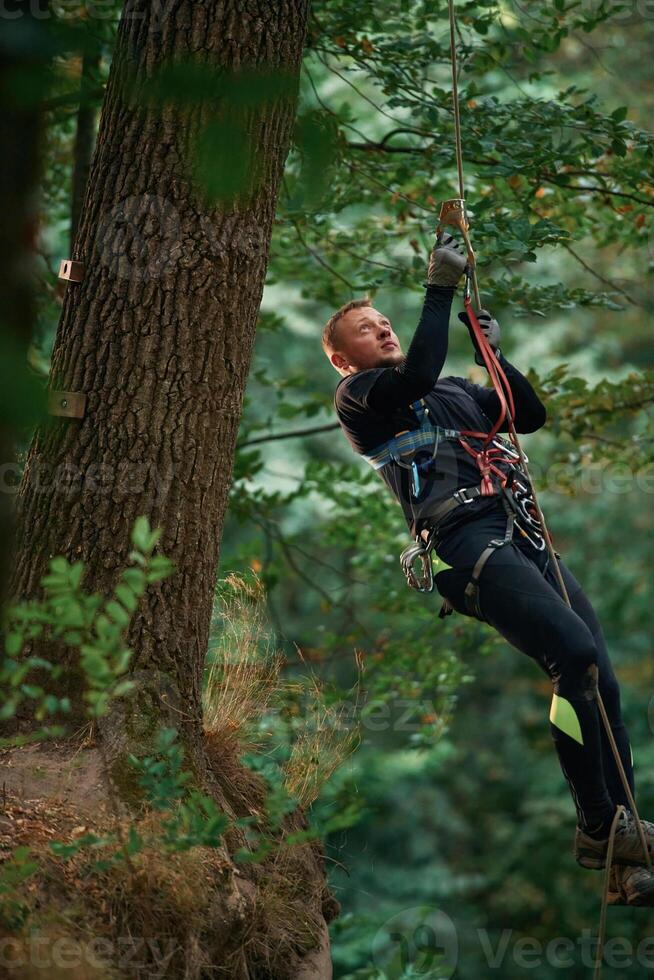 Activity, hanging on a rope. Man, is doing climbing in the forest by use of safety equipment photo