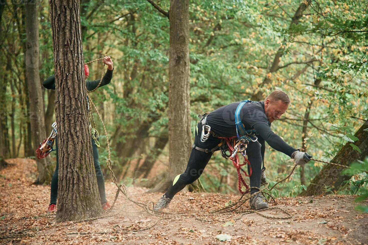 Standing on the ground and preparing. Man is doing climbing in the forest by use of safety equipment photo