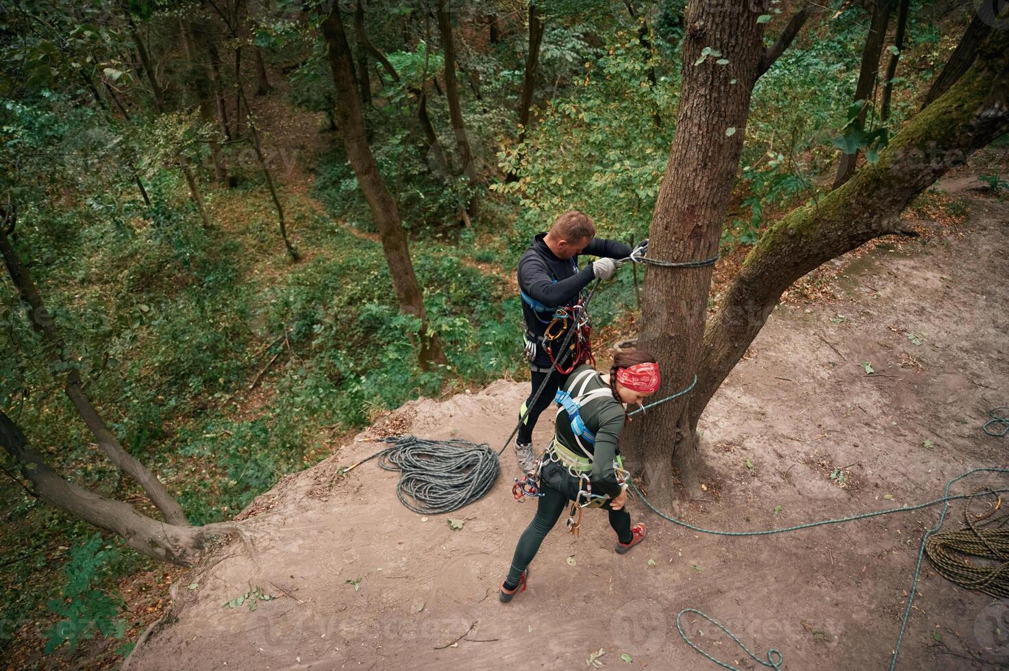 Top, view. Man and woman doing climbing in forest with use of safety equipment photo