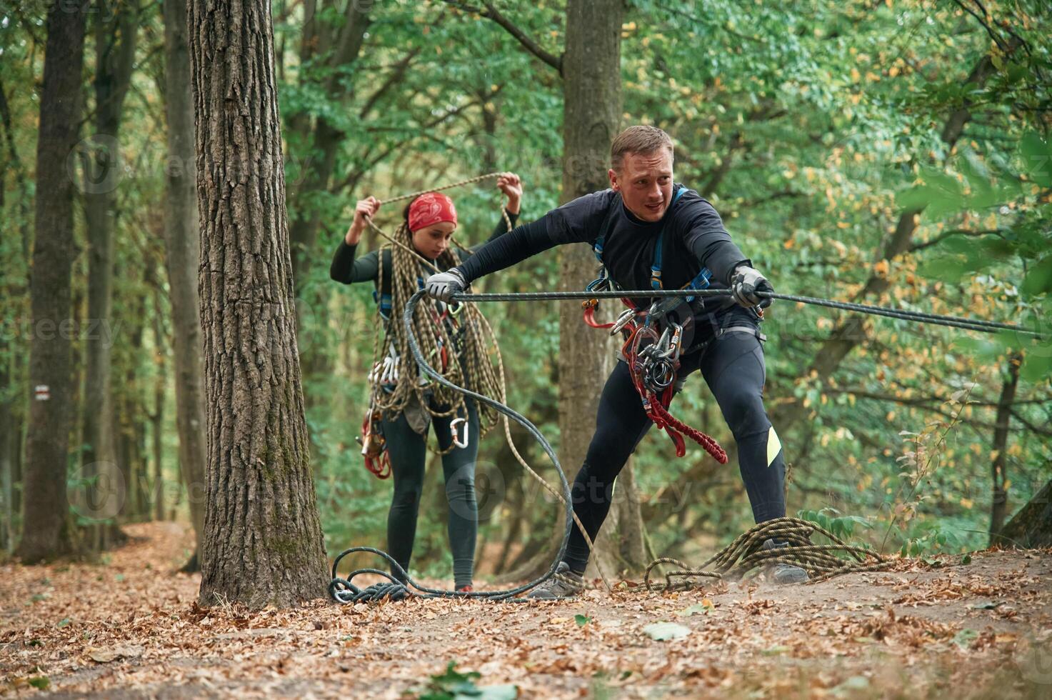 Standing together.. Man and woman, doing climbing in forest with use of safety equipment photo
