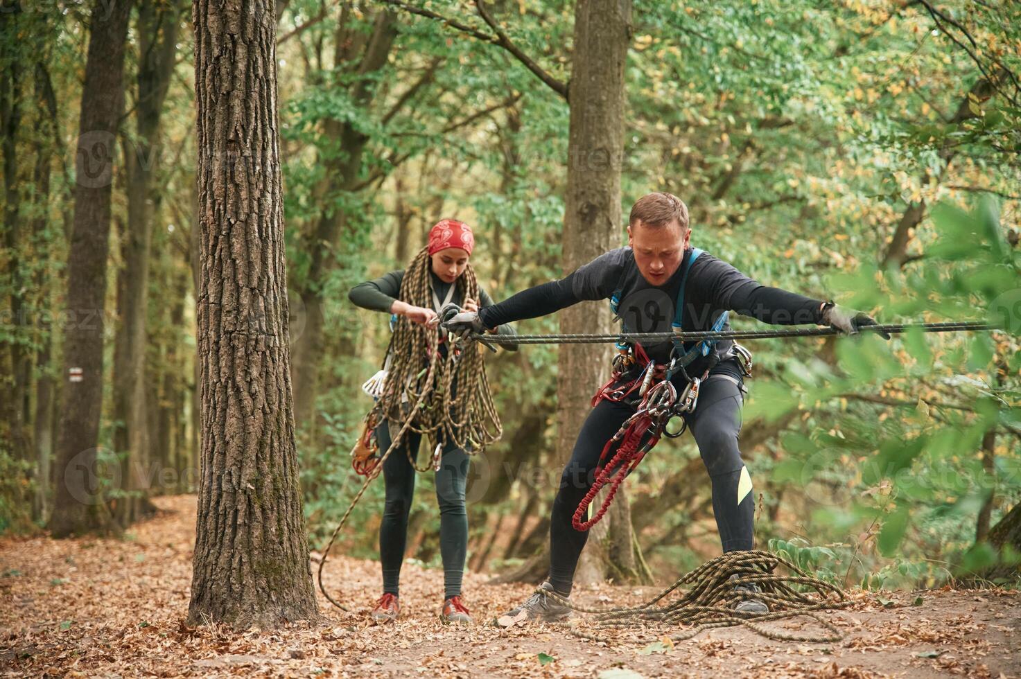 Standing together.. Man ,and woman doing climbing in forest with use of safety equipment photo