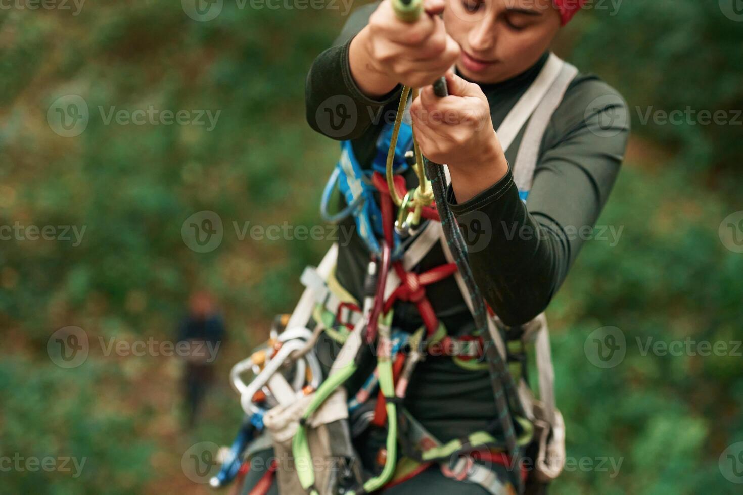 Front ,view. Woman is doing climbing in the forest by the use of safety equipment photo