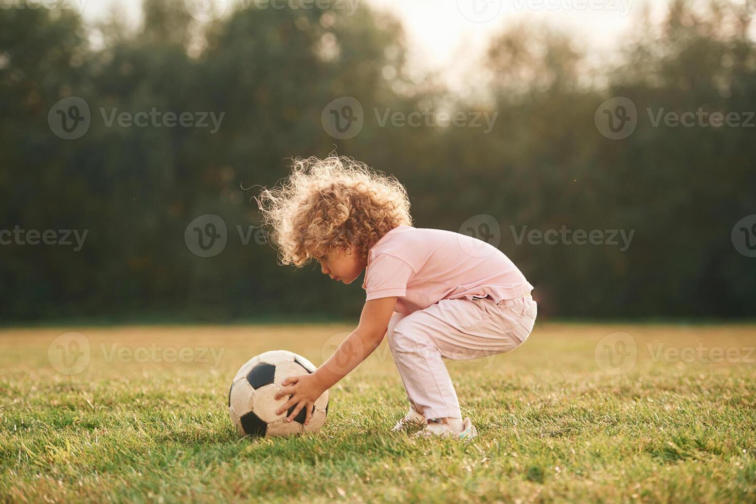 Soccer, ball ,is on the ground. Cute little girl with curly hair is playing on the field at daytime photo