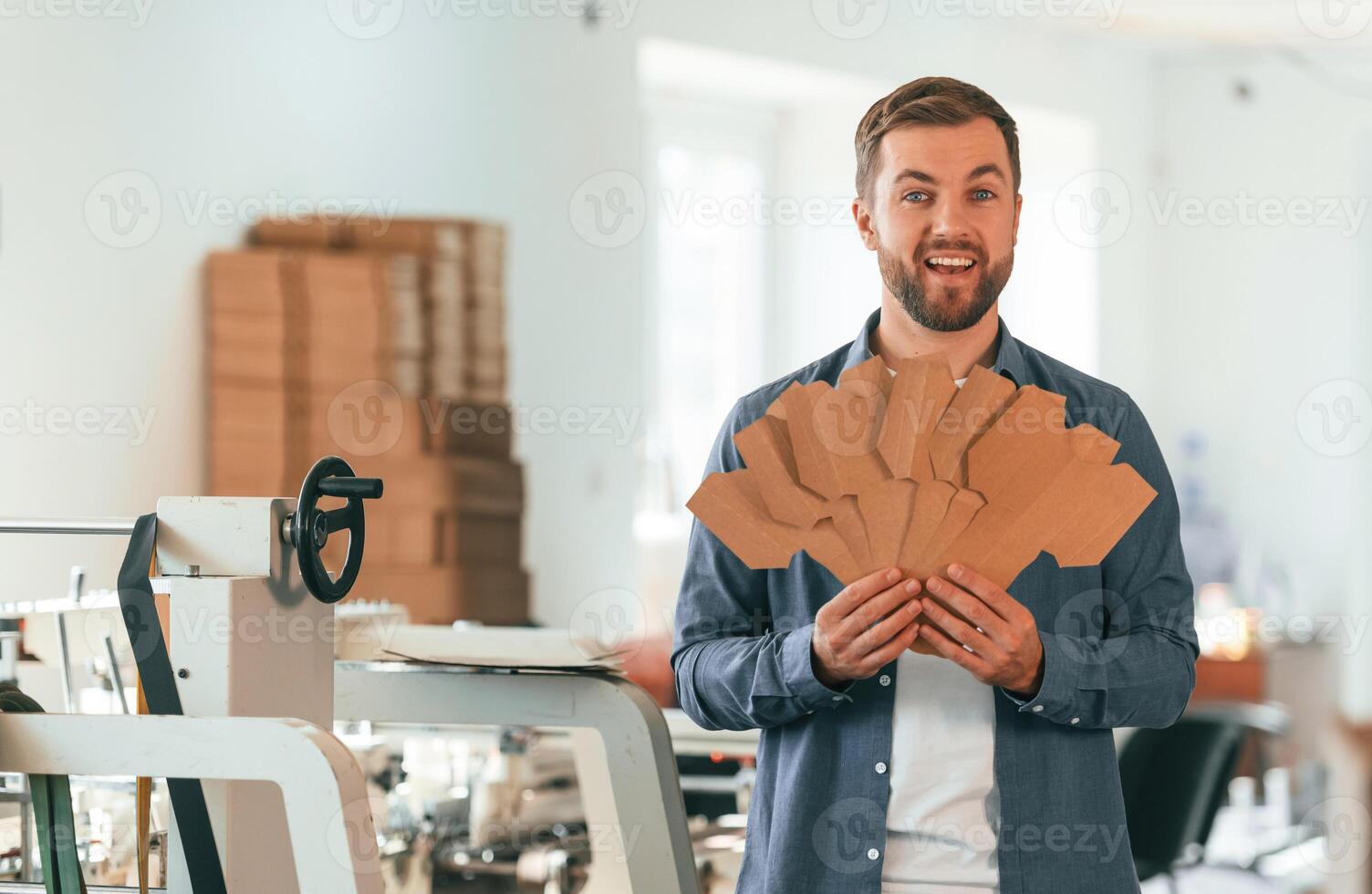 With ,,cardboards. Handsome man is working at the factory of creating eco boxes photo