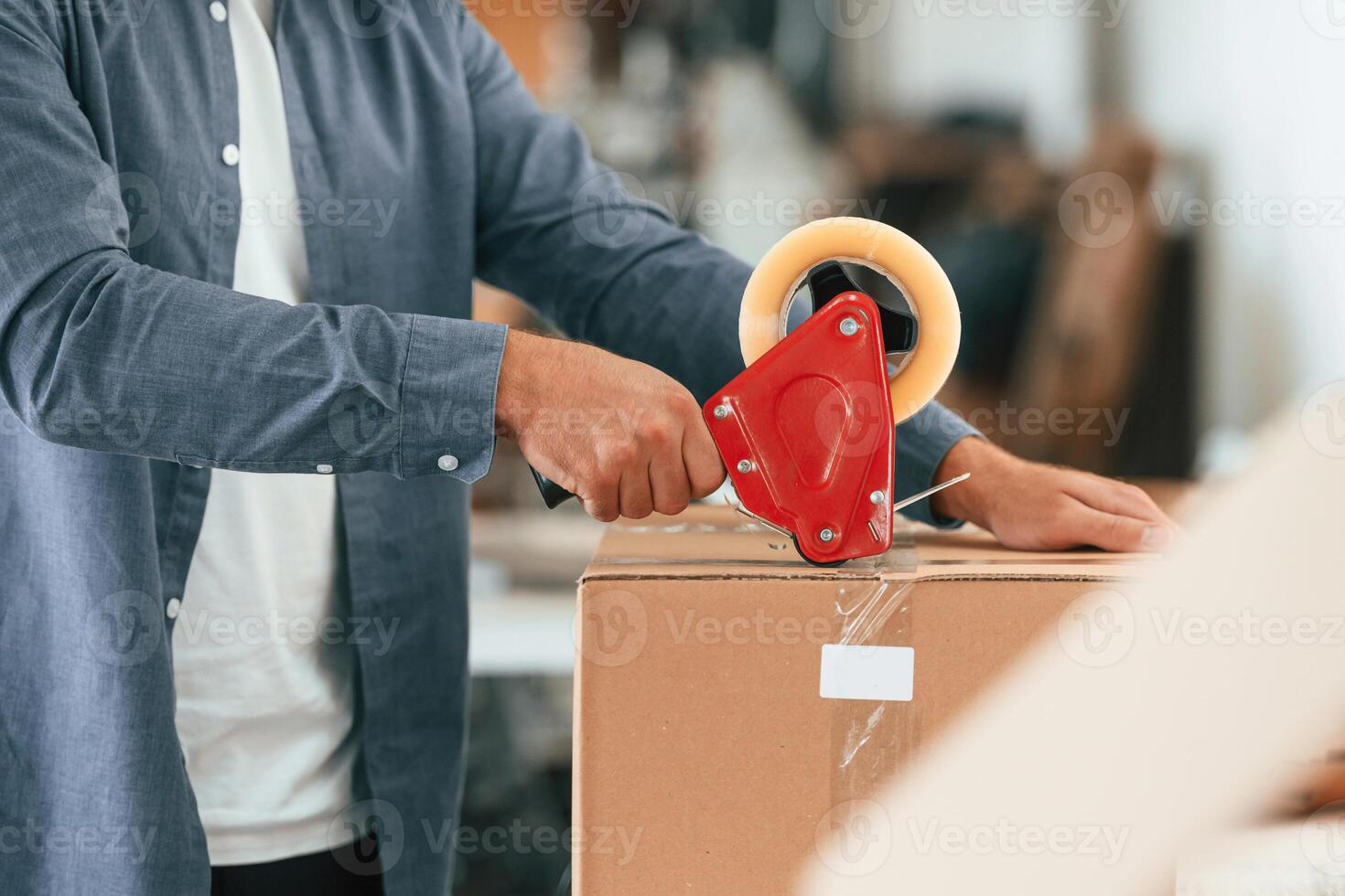 Using tape, packing the product. Handsome ,,man is working at the factory of creating eco boxes photo