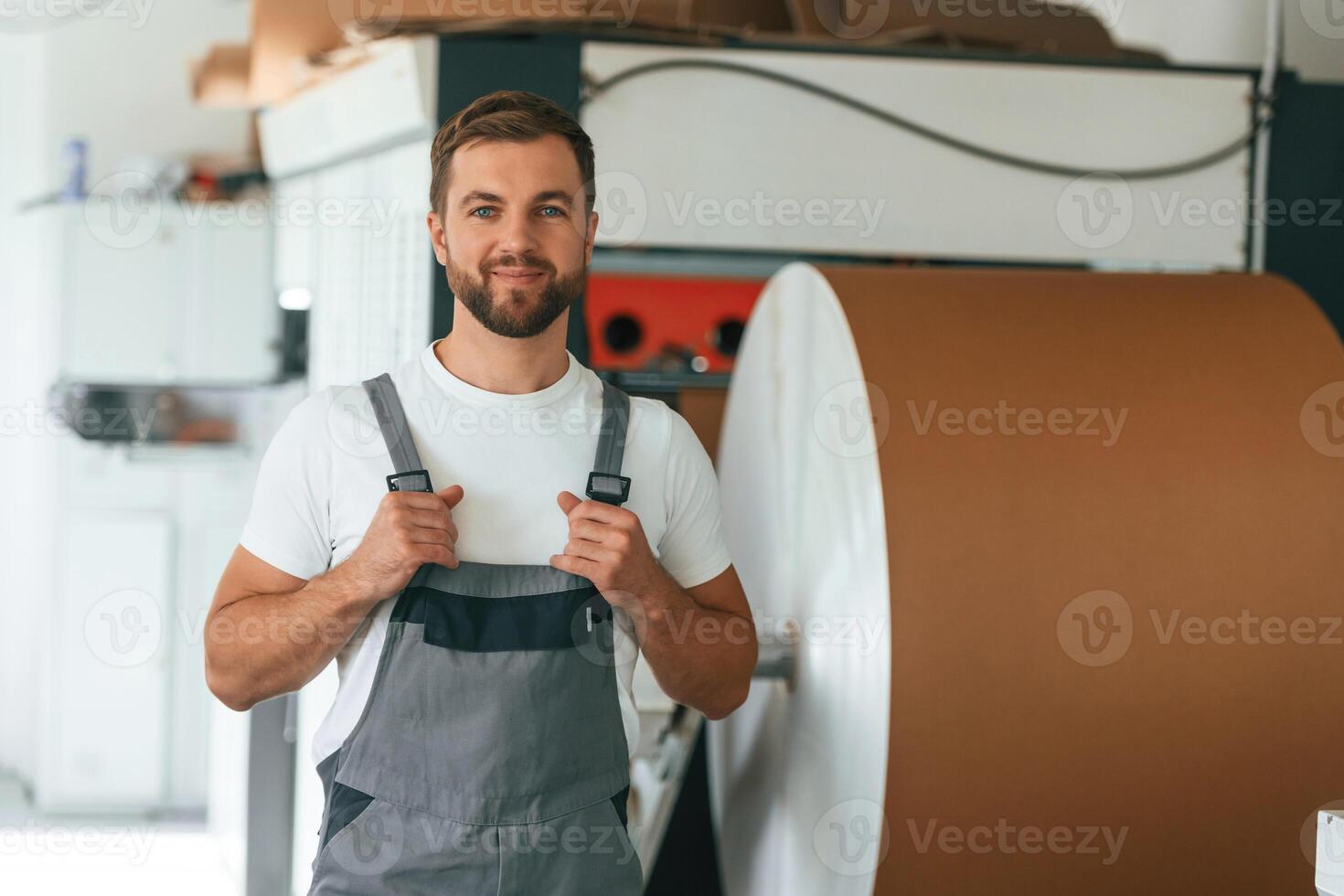 By, the rounded machine for making paper. Handsome man is working at the factory of creating eco boxes photo