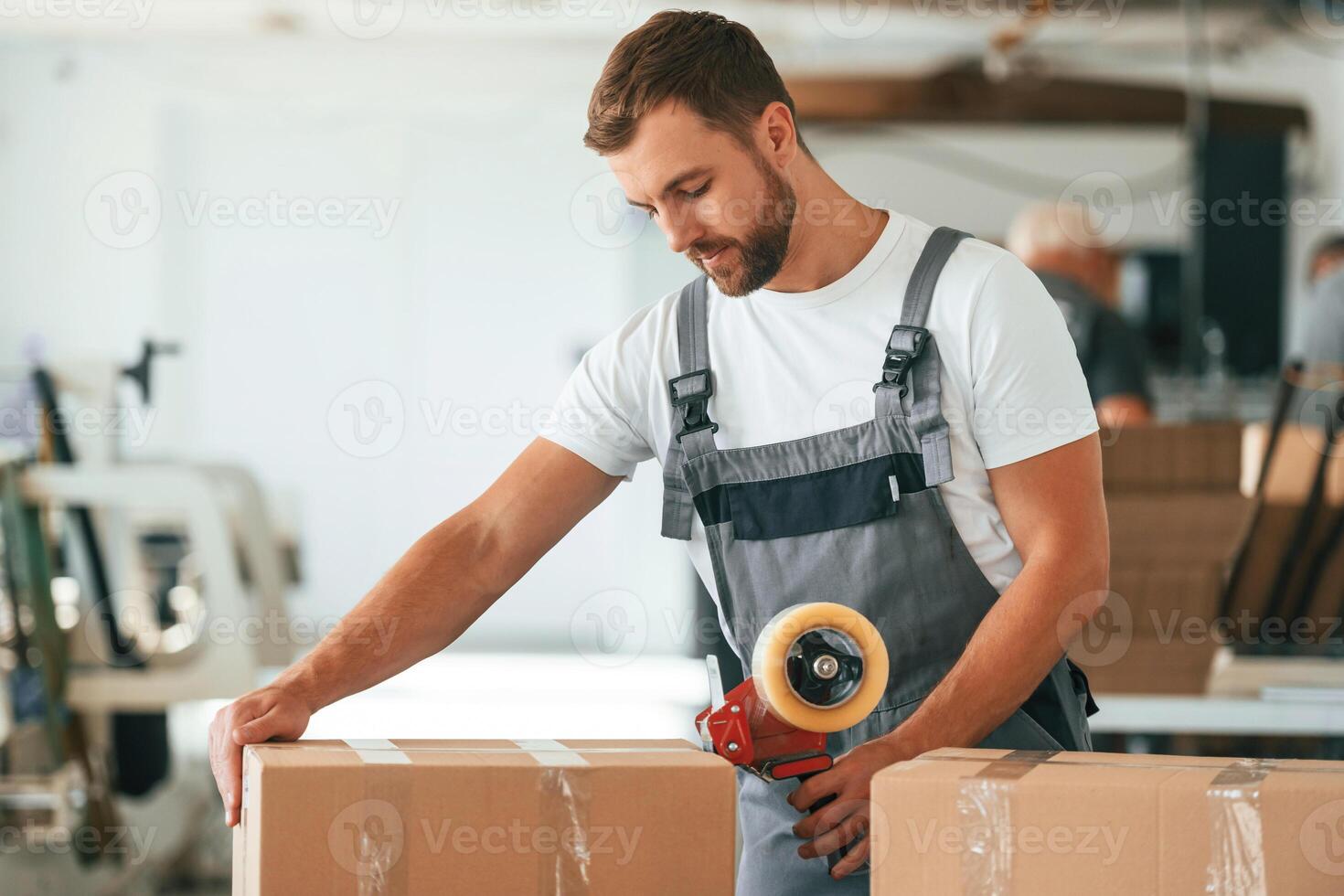 In greym uniform. Handsomem man is working at the factory of creating eco boxes photo