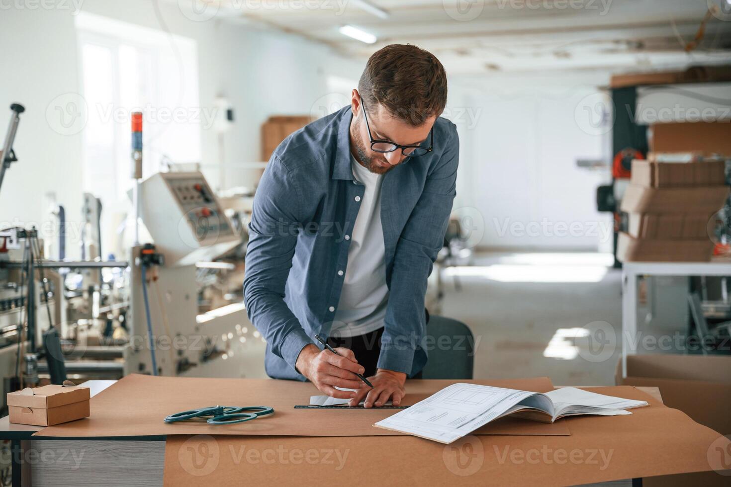 Standing, by the table.. Handsome man is working at the factory of creating eco boxes photo