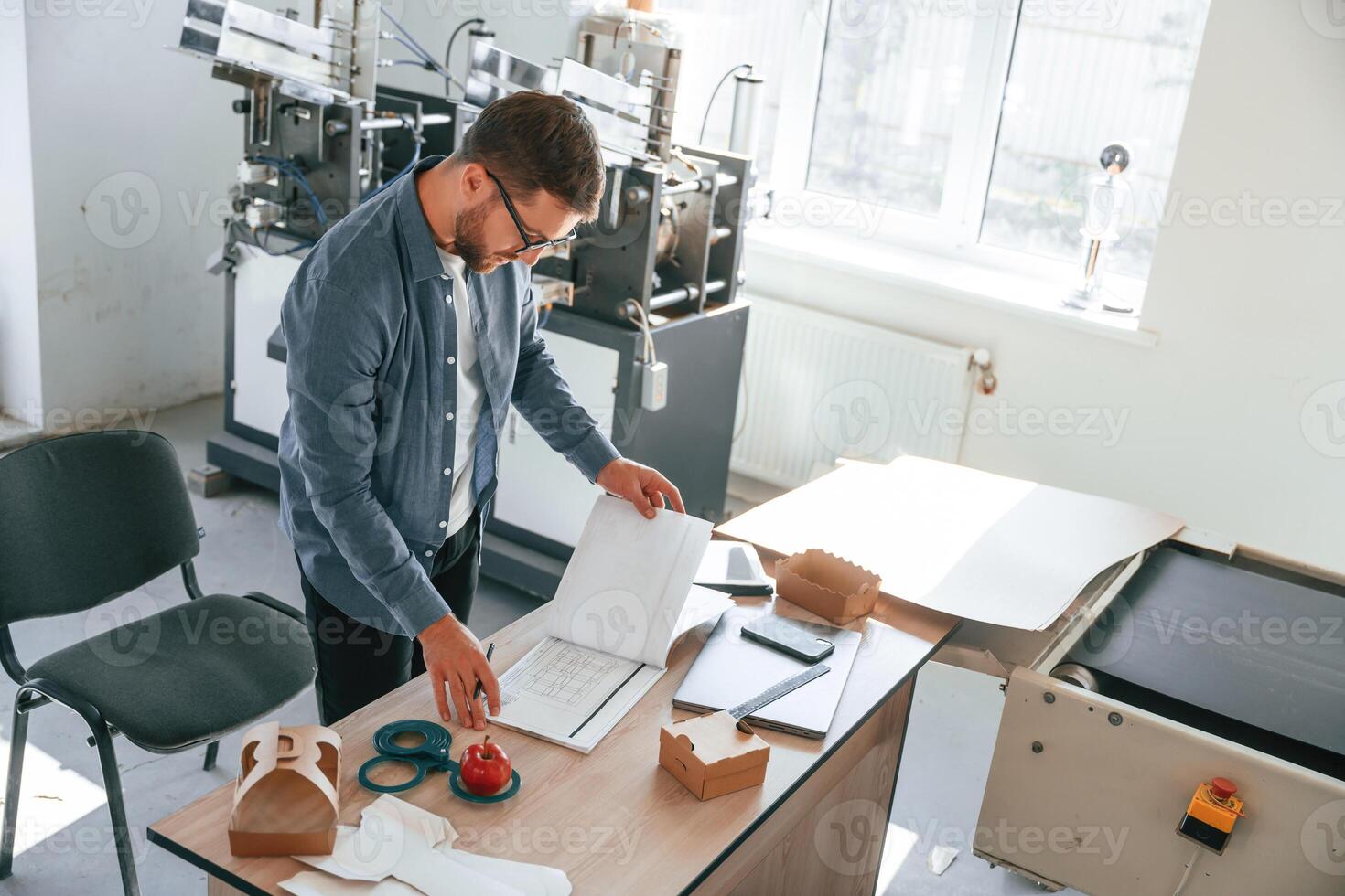 Standing,, by the table. Handsome man is working at the factory of creating eco boxes photo