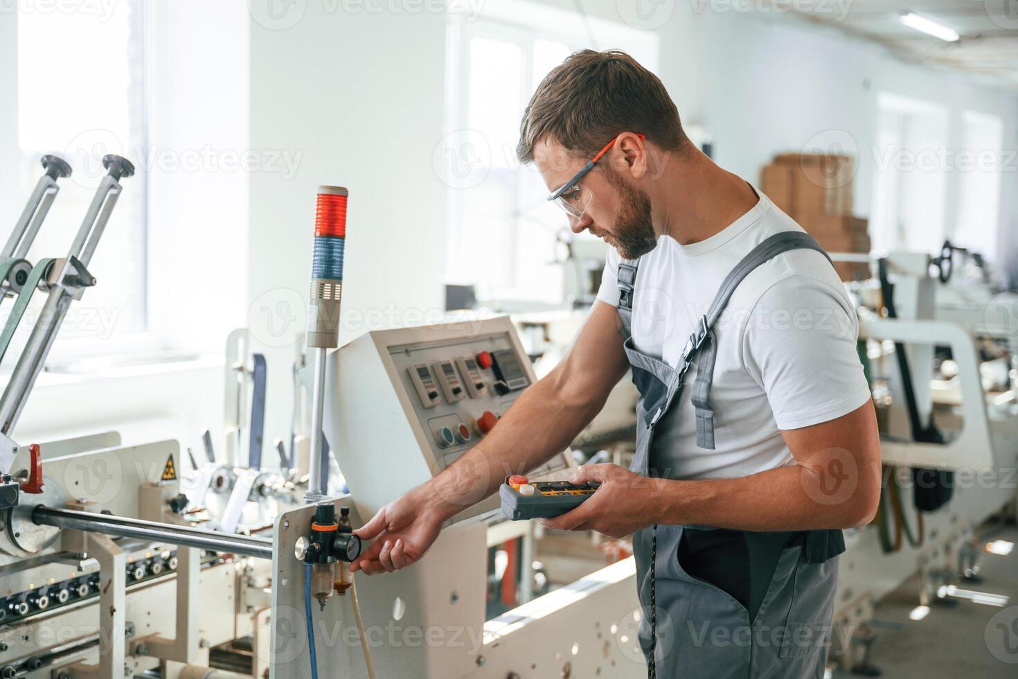 Standing, by the machine. Handsome man is working at the factory of creating eco boxes photo
