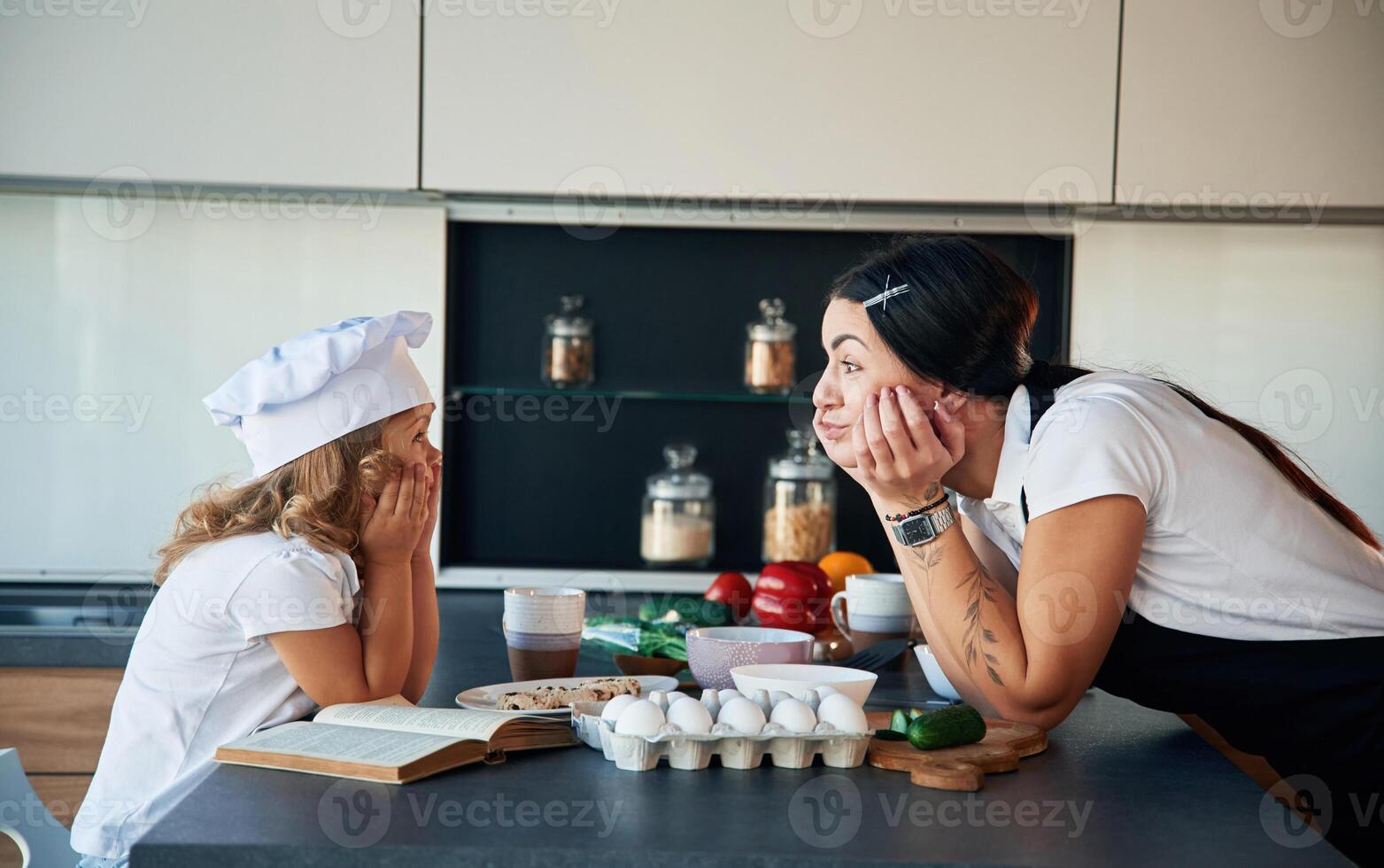 Standing, and,watching, at each other. Mother with her daughter are preparing food on the kitchen photo