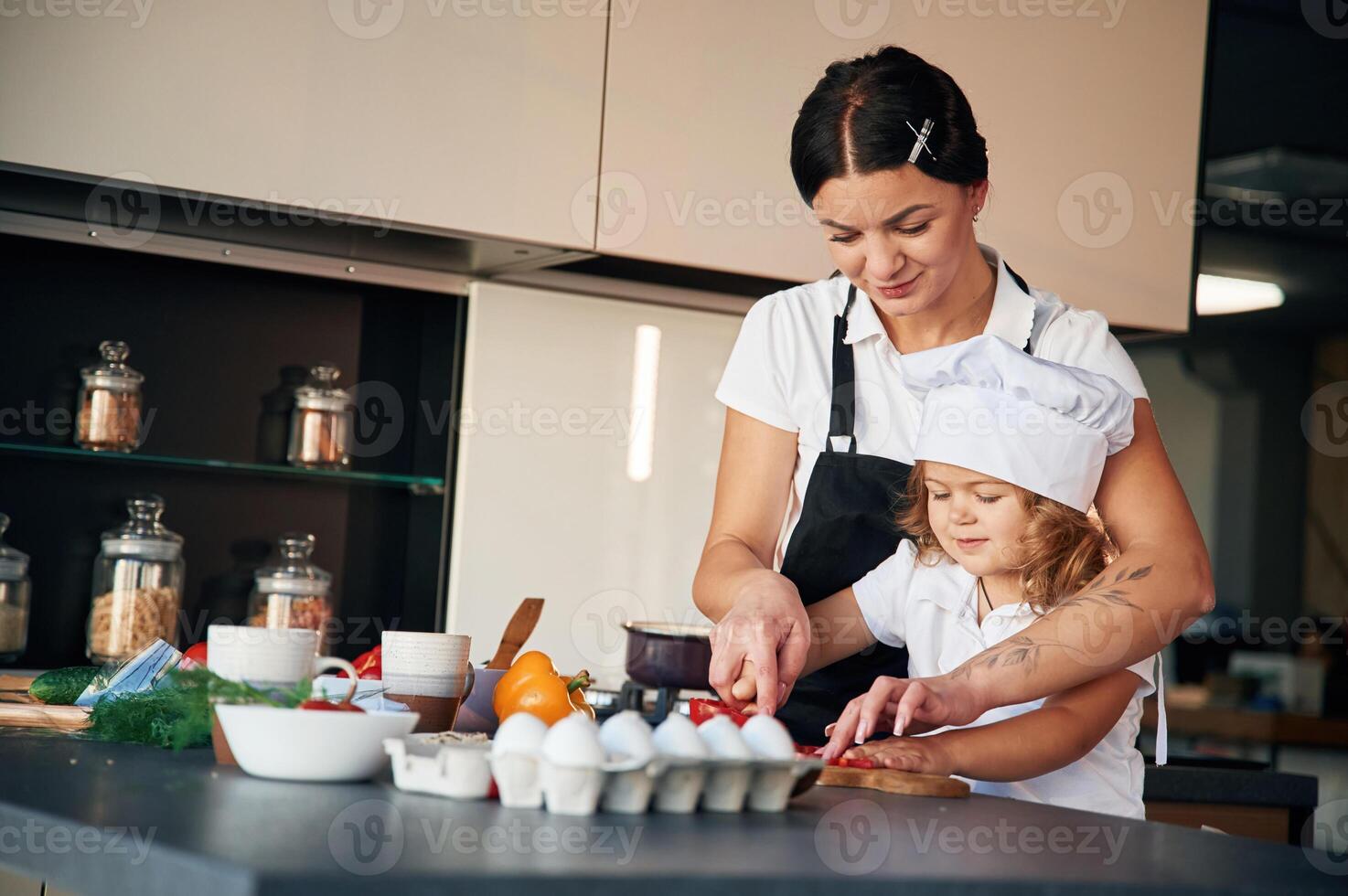 Woman ,is in ,apron, girl in chief hat. Mother with her daughter are preparing food on the kitchen photo