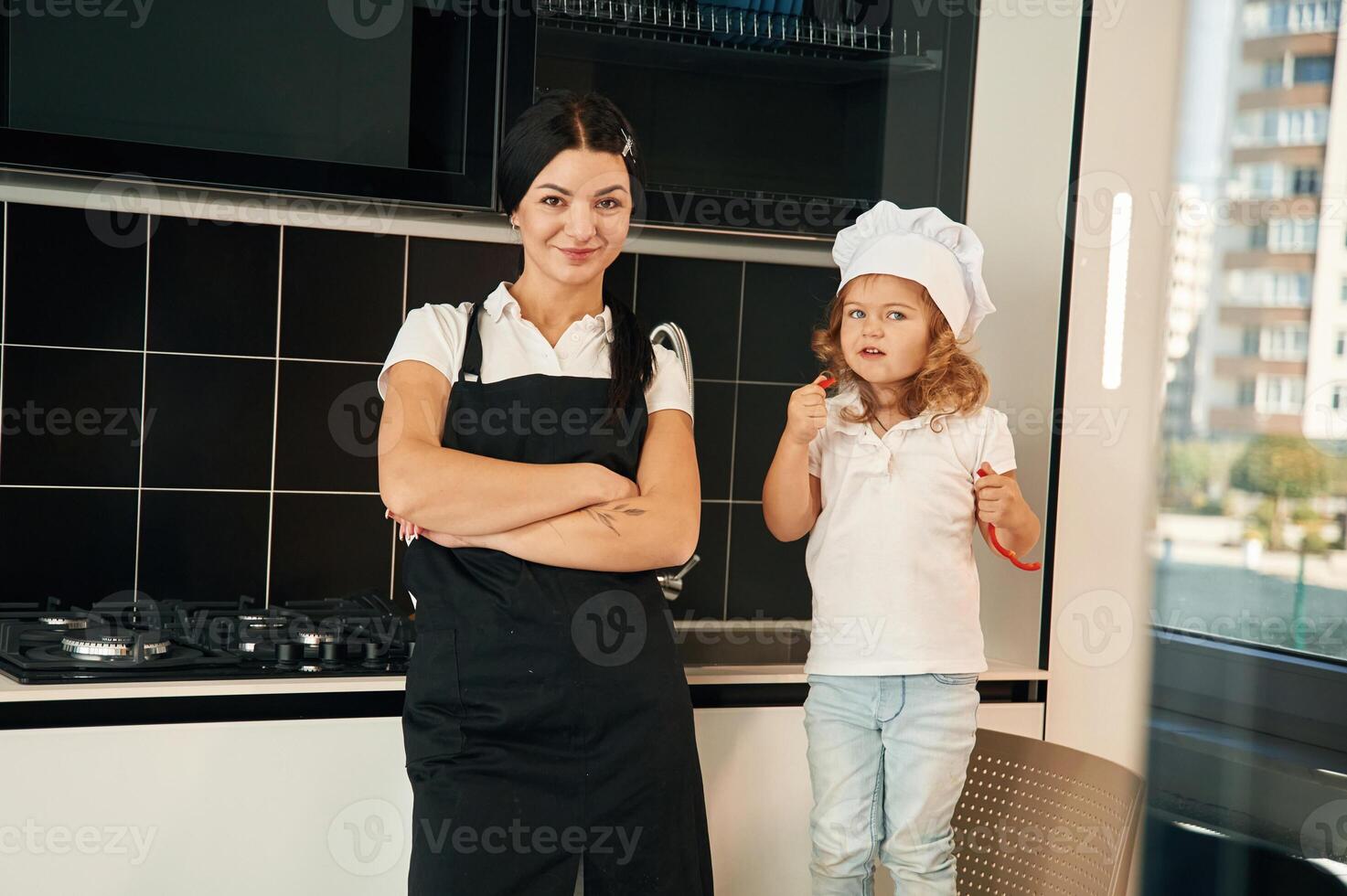 Standing, with ,arms crossed. Mother with her daughter are preparing food on the kitchen photo