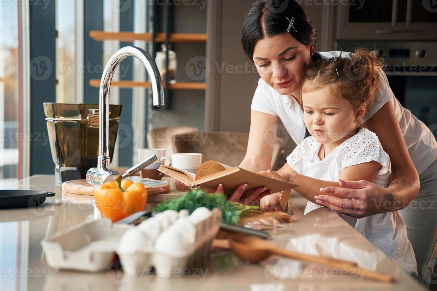 Reads the ,recipe. Mother with her daughter are preparing food on the kitchen photo