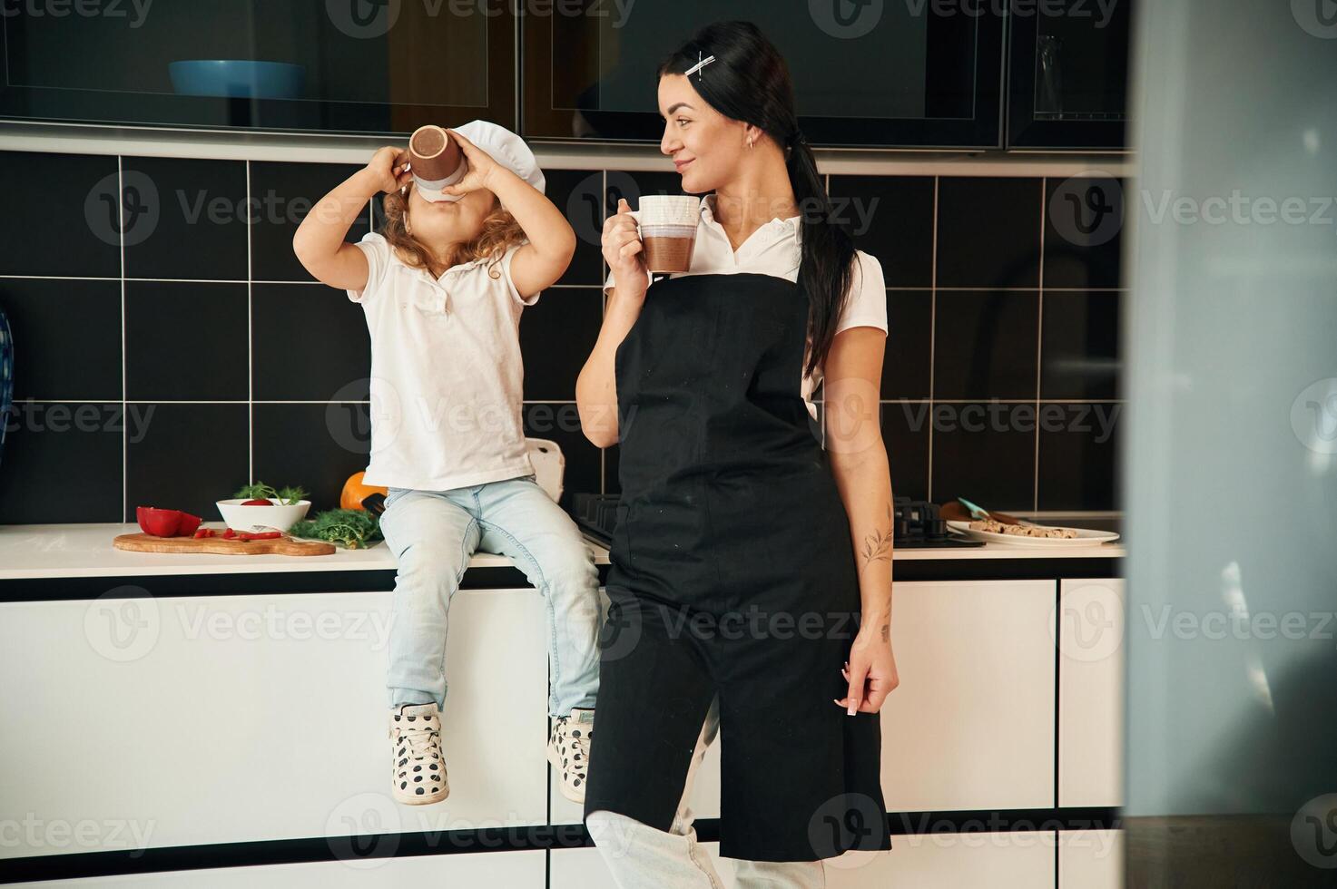 Drinking ,from the cups. Mother with her daughter are preparing food on the kitchen photo