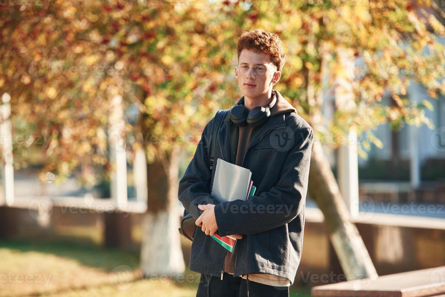 Standing, and holding notepad. Young student is outside the university, in black clothes photo