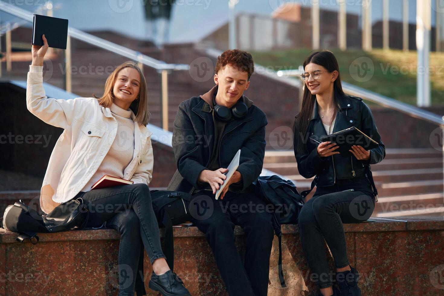 With, notepad. Three, young students are outside the university outdoors photo