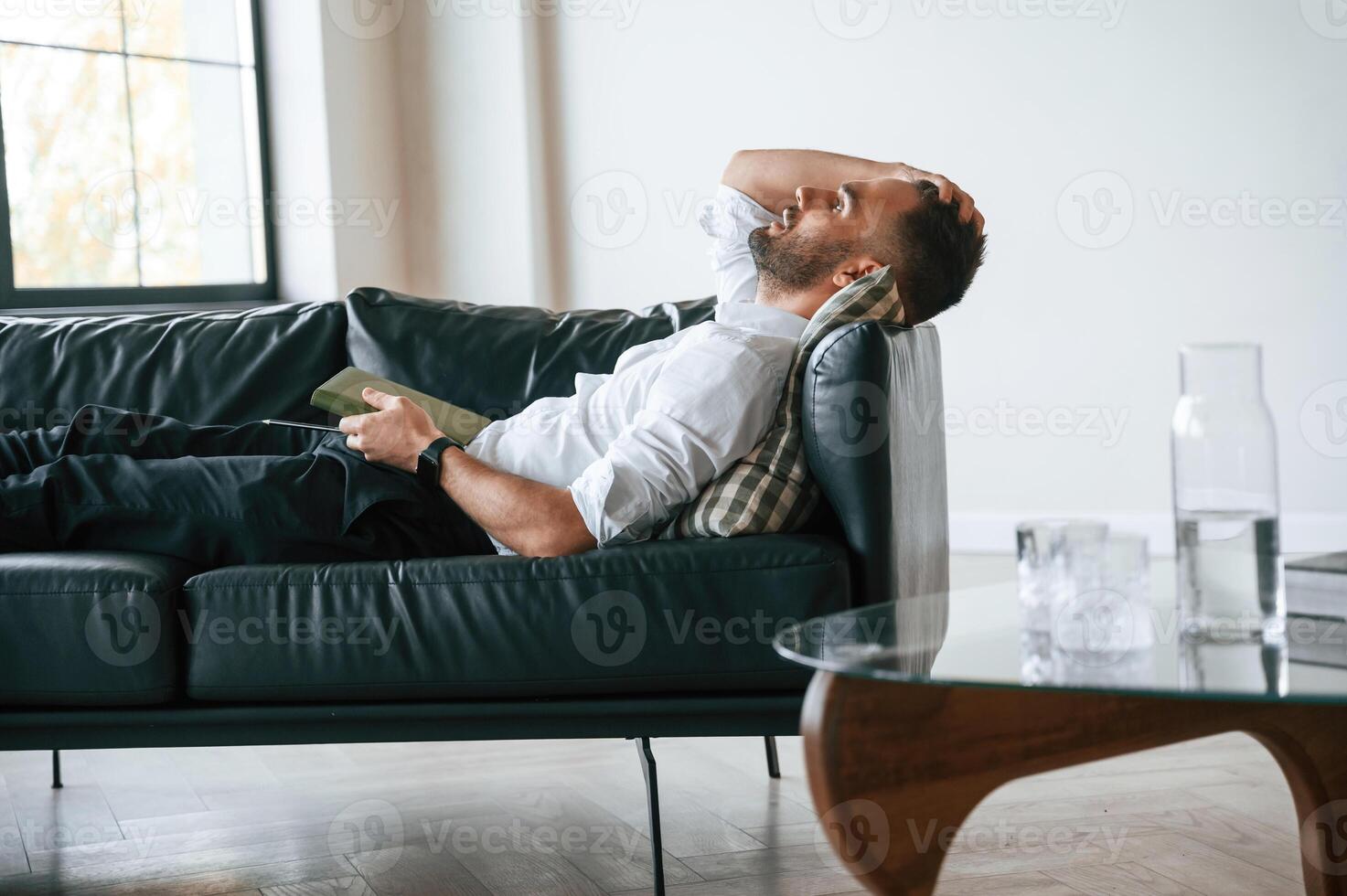 Tired man, in formal clothes is lying down on the black sofa photo