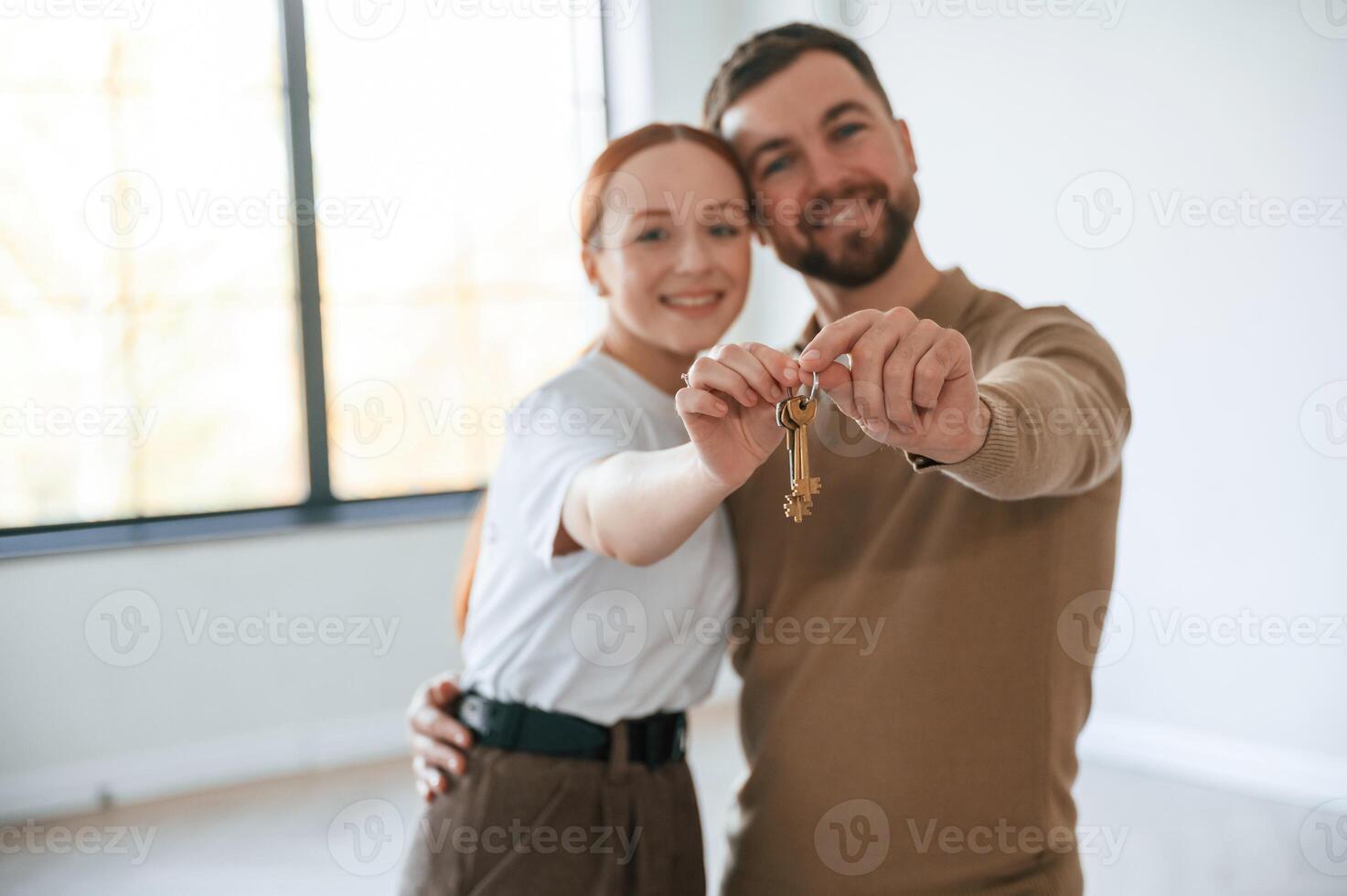 Happy couple, as new owners of the house holding the keys in hands photo