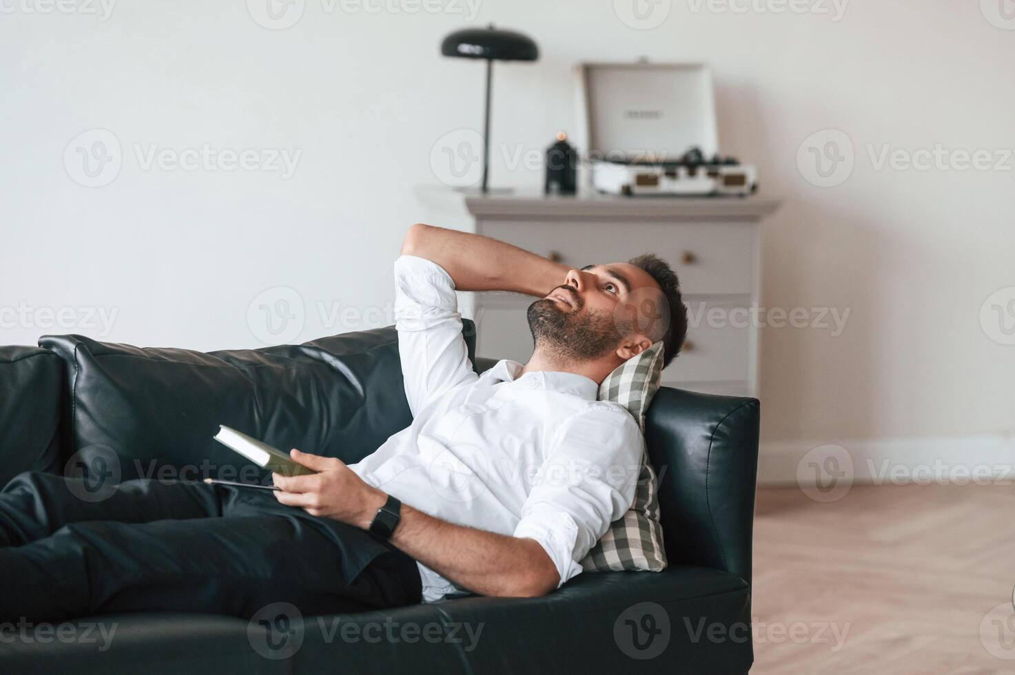 Tired, man in formal clothes is lying down on the black sofa photo