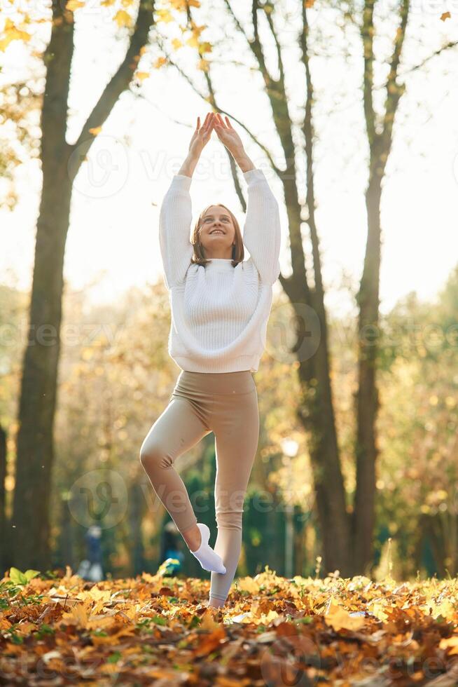 Illuminated by, sunlight. Young beautiful woman is doing yoga in the autumn park photo