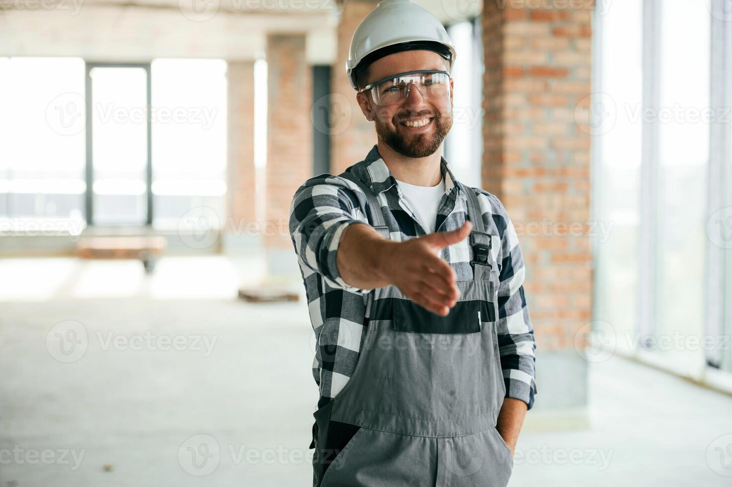 Giving the hand to shake, nice to meet you gesture. Construction worker in uniform in empty unfinished room photo