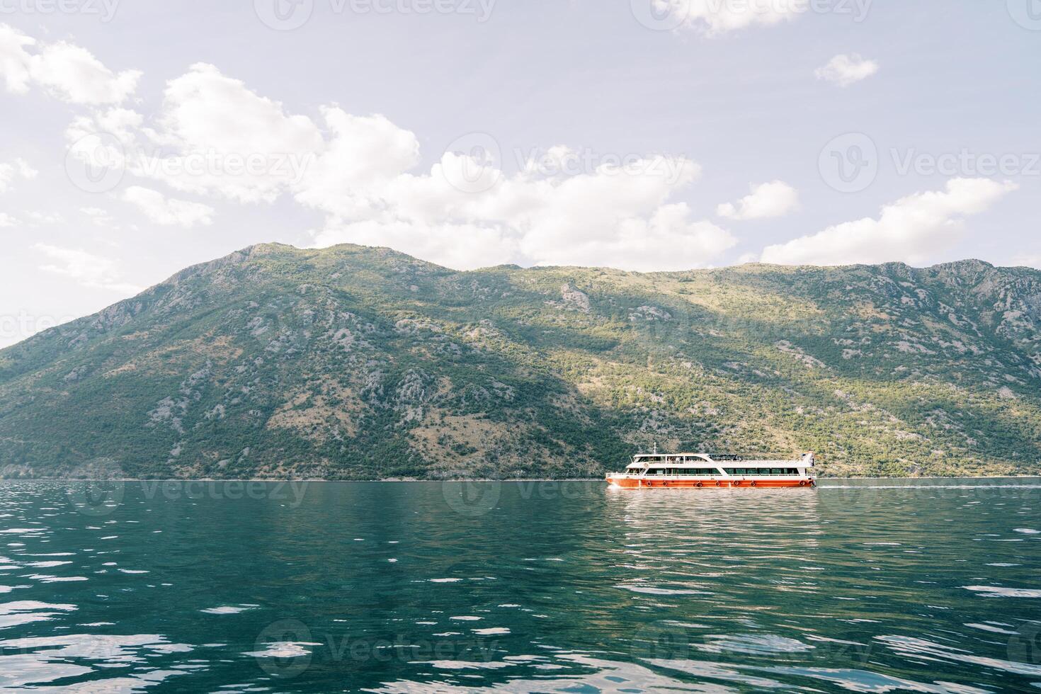 Colorful double-decker excursion ship sails on the blue sea along a high mountain ridge photo