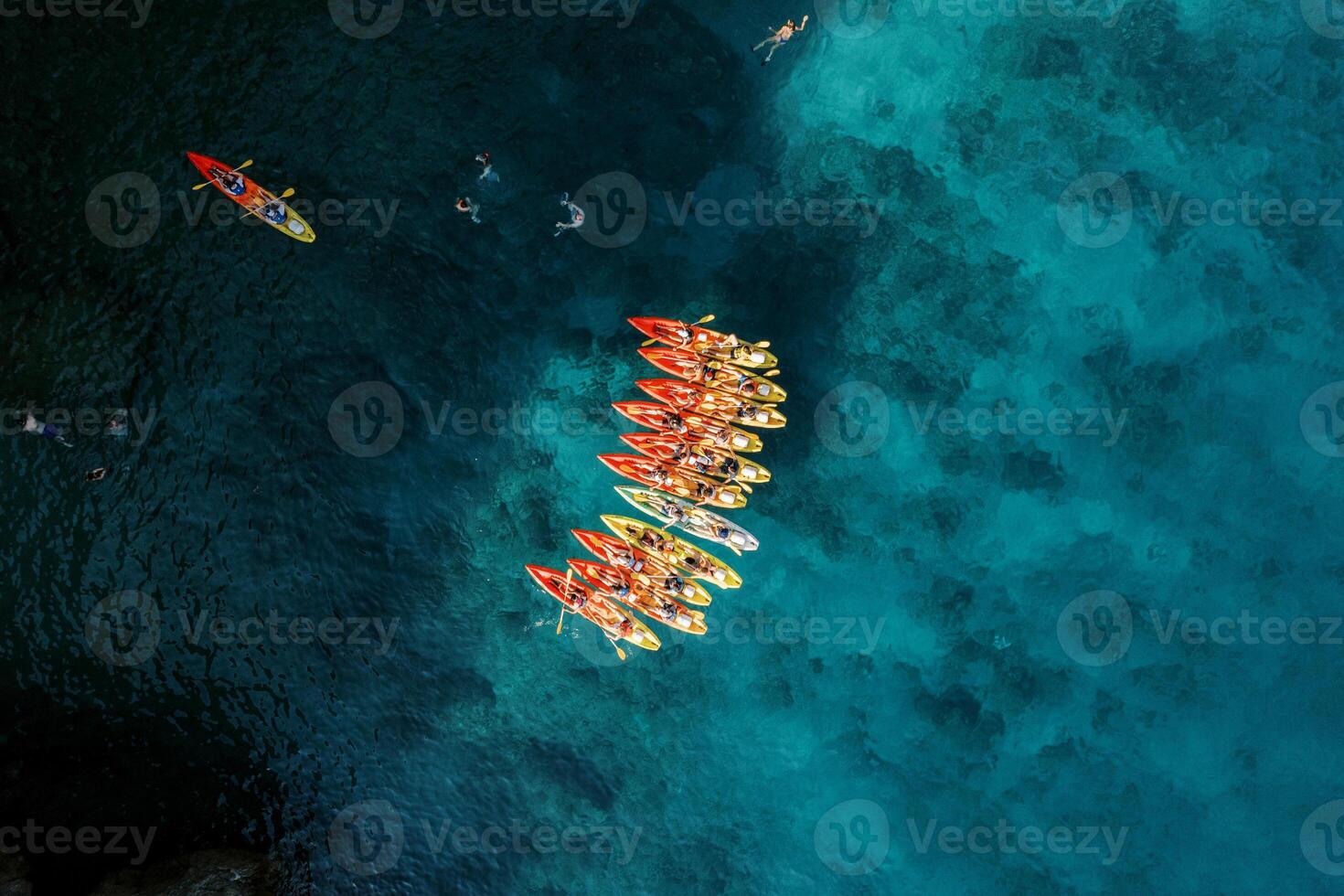 Captain boat sails towards a row of kayaks in the deep turquoise sea. Top view photo