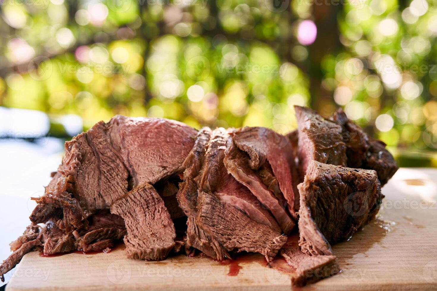 Slices of juicy roast beef lie on a cutting board on a glass table photo
