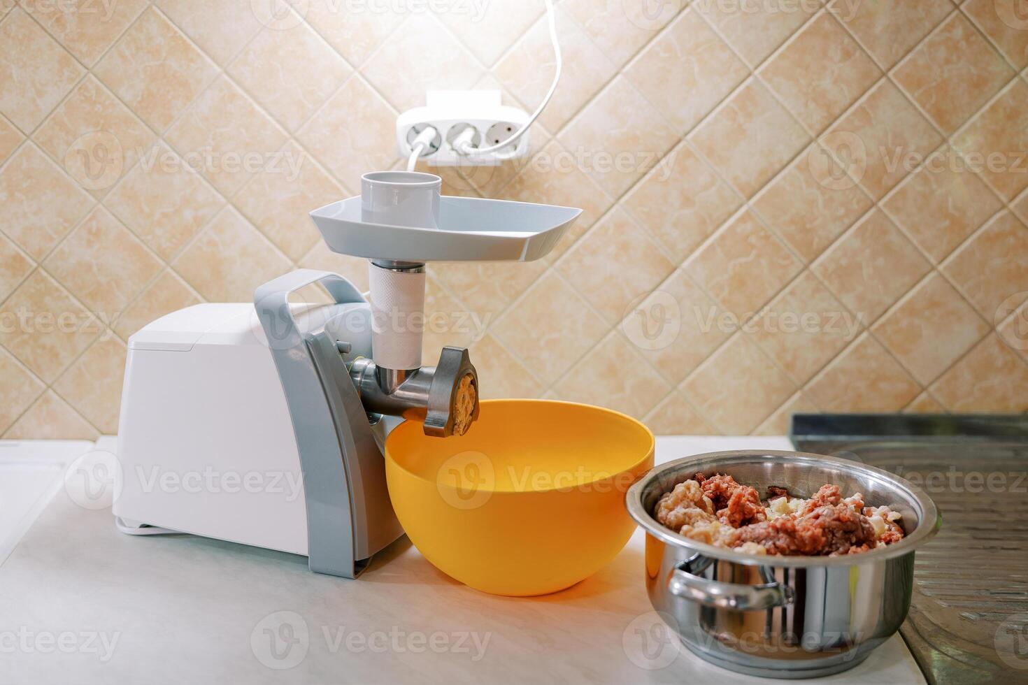 Electric meat grinder stands on a table next to a bowl and a pot of minced meat photo