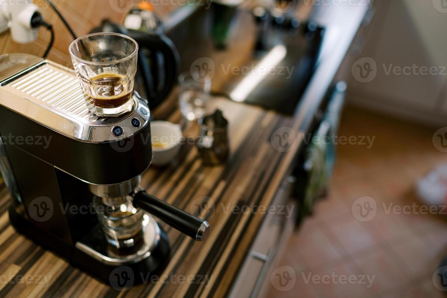 Glass of coffee stands on a carob coffee machine preparing coffee in a cup photo